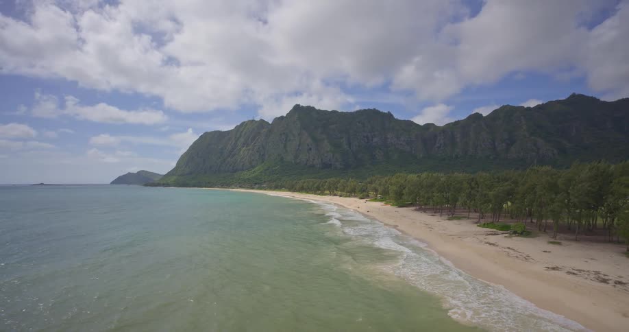 A beautiful, serene view of a sandy tropical beach with gentle ocean waves and lush green mountains in the background