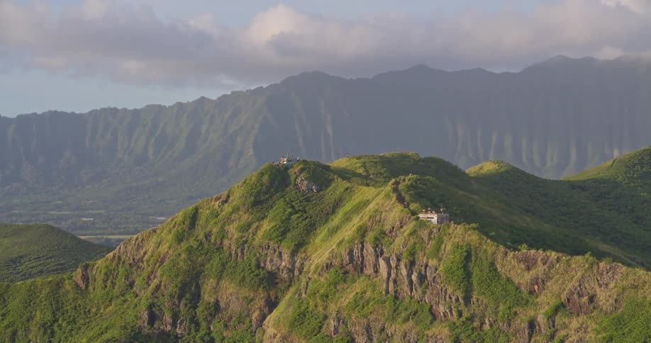 A cinematic aerial view slowly zooms in on the lush green mountains of the Kaiwa Ridge Trail in Lanikai, Oahu, Hawaii