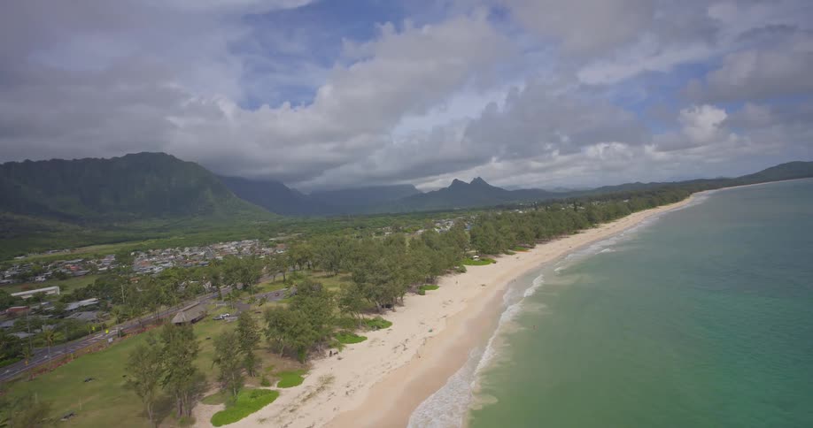 A breathtaking aerial flight along a pristine tropical coastline, showcasing the sandy beach, turquoise waters, and lush green mountains of Hawaii