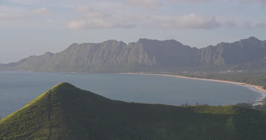 A slow aerial pullback reveals a breathtaking view of a tropical bay nestled between lush green mountains and the tranquil ocean