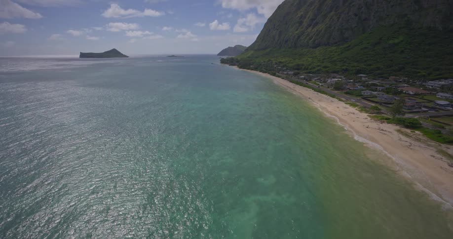 An aerial shot tilts up over the turquoise ocean to reveal a stunning tropical coastline with sandy beaches and lush green mountains