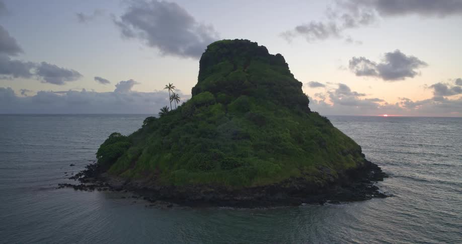 A serene, wide shot of a lush green tropical island, known as Chinaman's Hat in Hawaii, during a beautiful sunrise