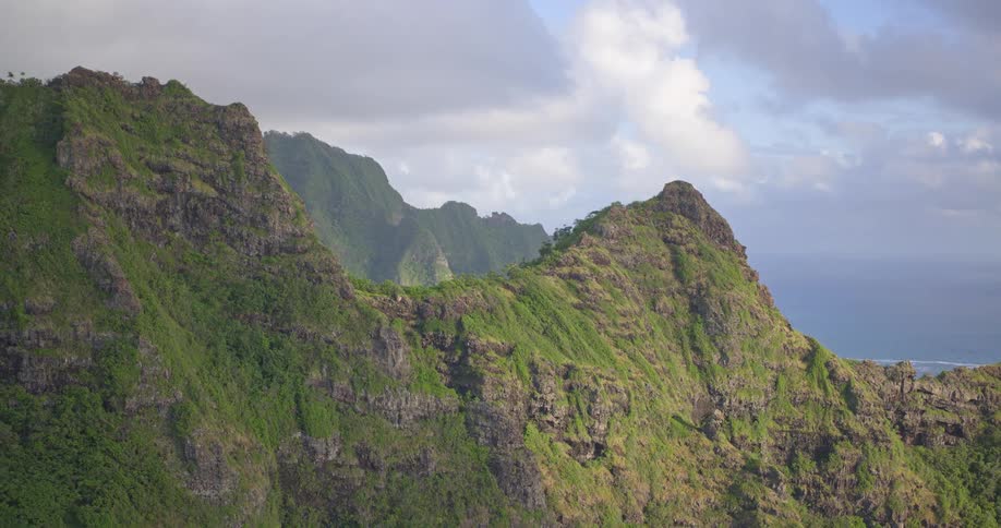 Majestic aerial shot slowly pulls back from a verdant, rocky mountain peak on a tropical coast