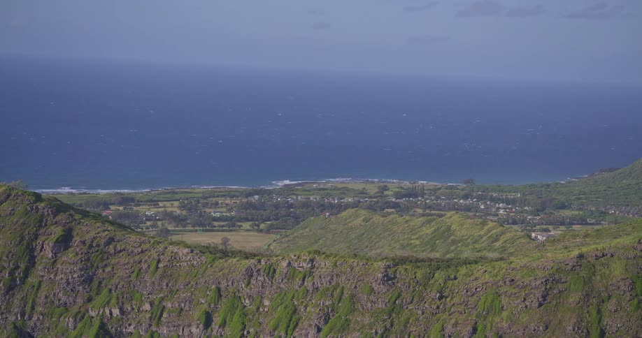 Slowly panning out from a high-angle view of a tropical island's lush green coastline and the vast blue sea