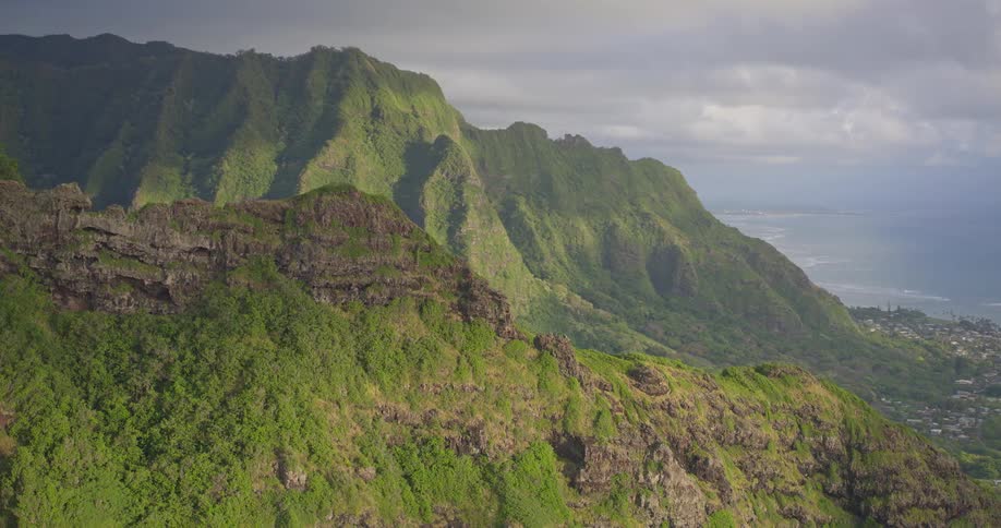 A breathtaking aerial pan reveals the majestic and verdant Koolau Mountain Range on the island of Oahu, Hawaii, with its rugged cliffs descending towards the Pacific Ocean