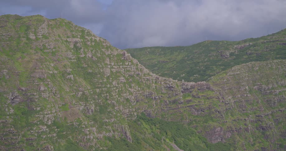 A slow zoom out reveals a vast and rugged green mountain range under a dramatic cloudy sky