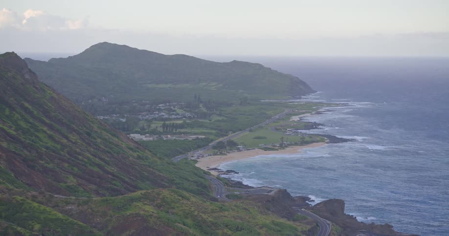 A scenic, wide-angle view of a lush green Hawaiian coastline with a winding road and sandy beach