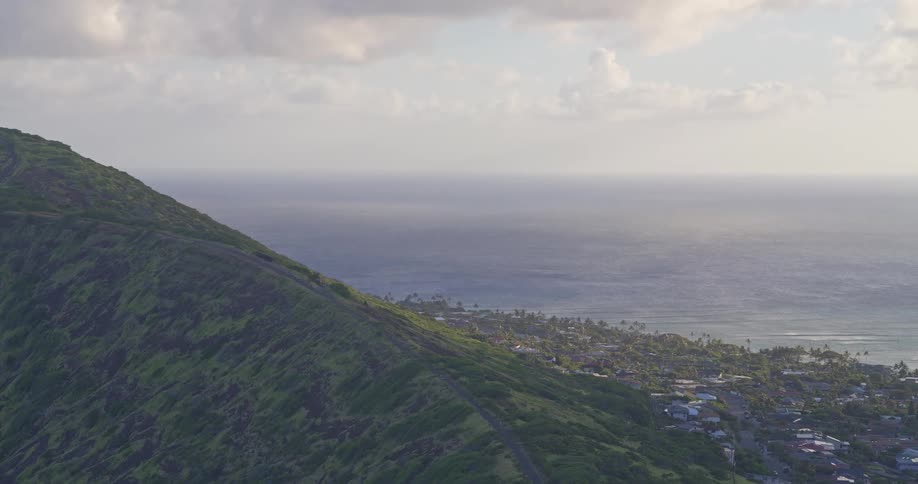 A tranquil wide shot of a verdant coastal mountain overlooking a seaside community and the vast blue ocean