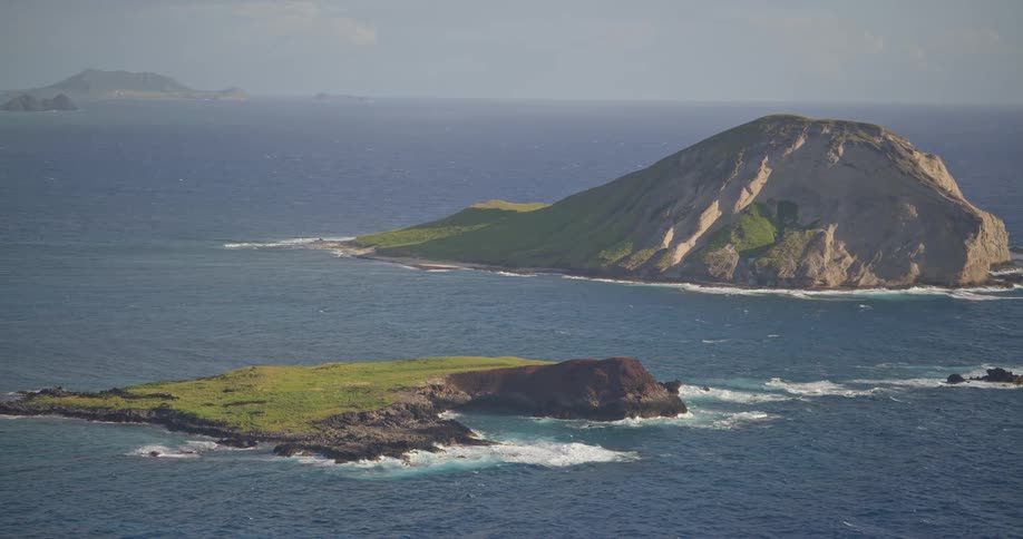 An aerial view slowly zooms out from the lush, volcanic islands of Manana and Kaohikaipu, revealing the vast expanse of the Pacific Ocean off the coast of Oahu