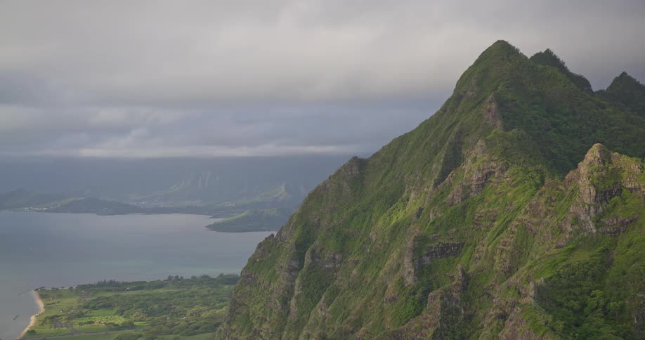 A stunning, wide view of a majestic green mountain range overlooking the ocean under a cloudy sky