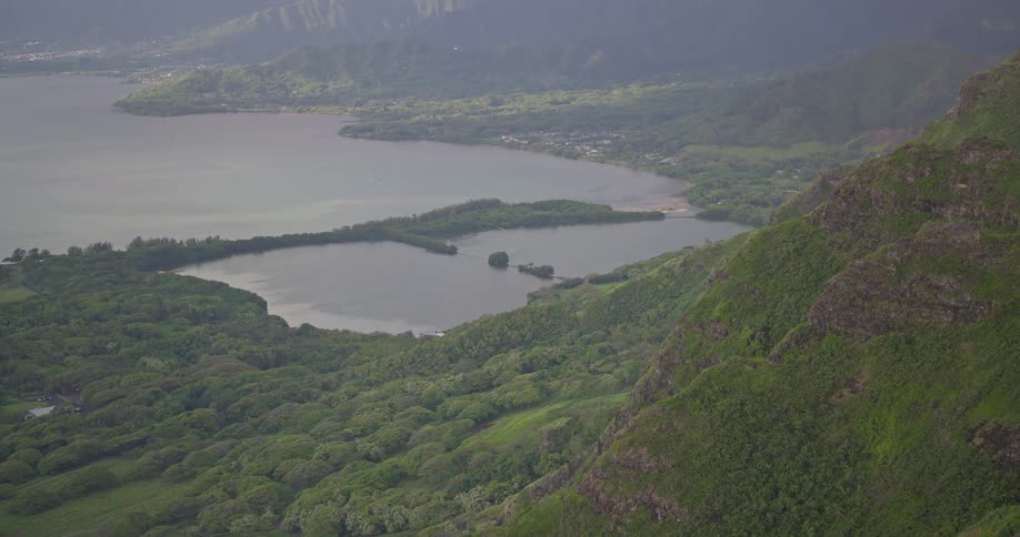 A serene high-angle view of a Hawaiian bay and ancient fishpond surrounded by lush green mountains on a hazy day