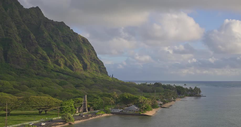 A serene aerial shot captures the majestic Kualoa mountain range descending into the tranquil waters along the coast of Oahu, Hawaii