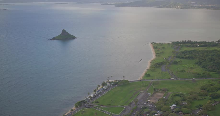 An expansive aerial view of the iconic Mokoliʻi island, also known as Chinaman's Hat, and the lush green coastline of Kualoa Regional Park in Oahu