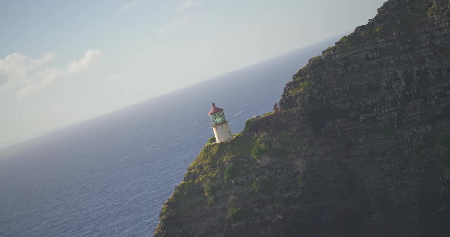 A canted angle shot slowly zooms out and levels, revealing a scenic lighthouse on a dramatic cliff overlooking the vast ocean
