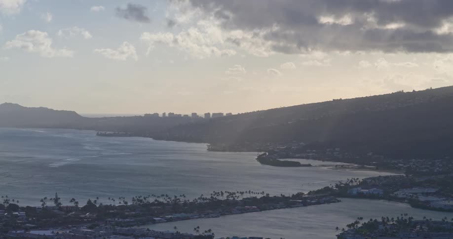 Sunbeams break through the clouds over a picturesque bay, illuminating the water and the distant Honolulu skyline