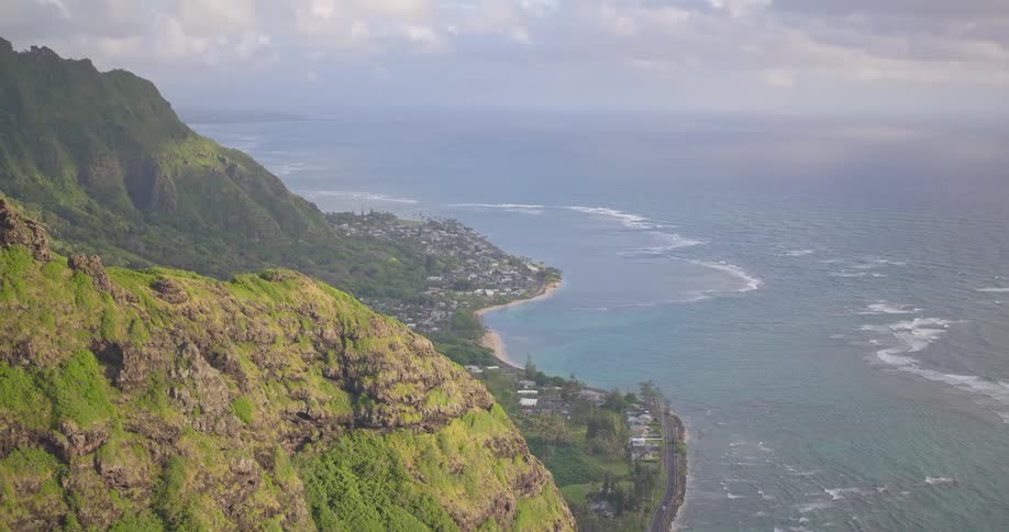 A stunning high-angle shot pulls back from the Hawaiian coastline to reveal the majestic, lush green Koolau Mountain Range overlooking the Pacific Ocean