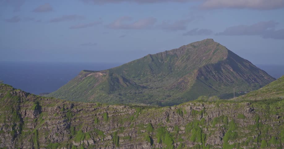 A stunning aerial pullback reveals the lush green Koko Head Crater, a coastal town, and the vast Pacific Ocean on Oahu, Hawaii