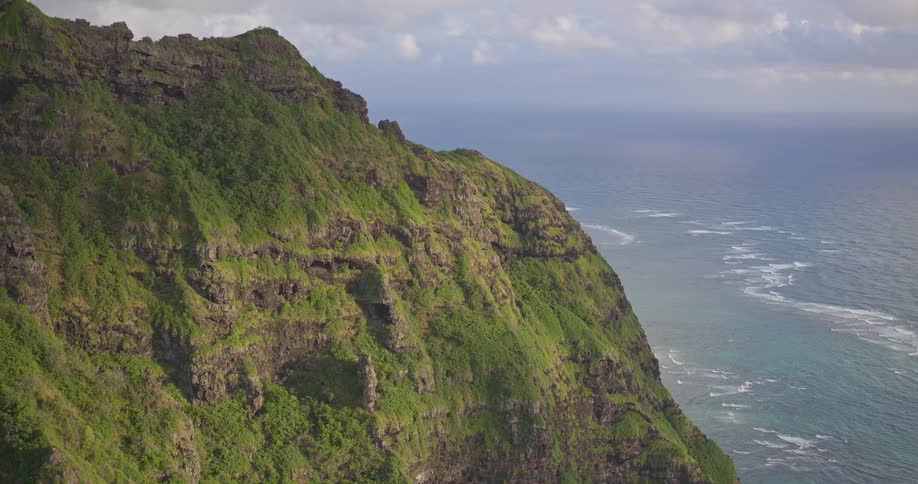 A majestic aerial view reveals the steep, green cliffs of a tropical island dropping dramatically into the deep blue ocean