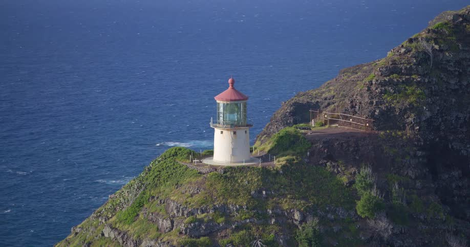 A slow zoom out from the historic Makapuu Point Lighthouse perched on a rugged, green cliff above the deep blue Pacific Ocean on Oahu, Hawaii