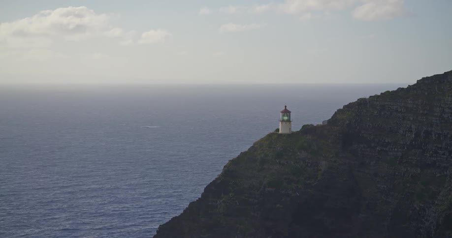 A serene, static shot of a lighthouse with a flashing green light perched on a rugged cliffside overlooking the vast ocean