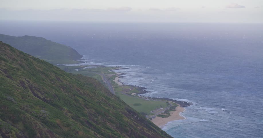 A majestic high-angle view reveals a verdant tropical mountain range cascading down to meet the deep blue ocean coastline