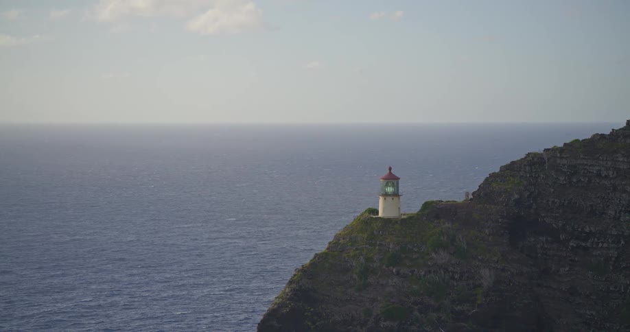 A picturesque lighthouse stands sentinel on a rugged cliff overlooking the vast, deep blue ocean