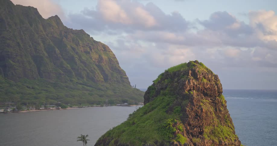 Stunning aerial footage gracefully orbits the iconic Mokoliʻi island, revealing the majestic Koʻolau mountain range and the tranquil waters off Oahu, Hawaii
