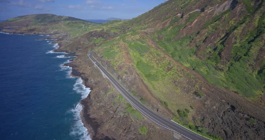 An aerial shot captures the breathtaking beauty of a winding highway along the rugged, green coastline of a tropical island