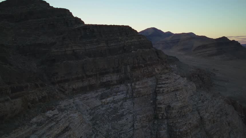 A slow aerial view captures the layered rock formations of a desert mountain range at twilight