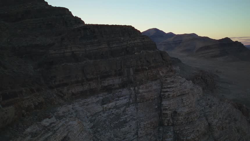 A slow aerial view captures the layered rock formations of a desert mountain range at twilight