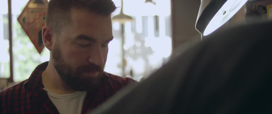 A bearded man staring at something and speaking as another person cleans his hand with a gauze pad