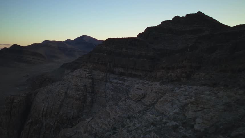 An aerial view of a rugged mountain landscape silhouetted against the sky at dawn