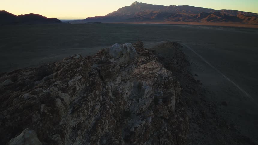 A slow push-in shot along a rugged, rocky ridge overlooking a vast desert landscape at sunrise