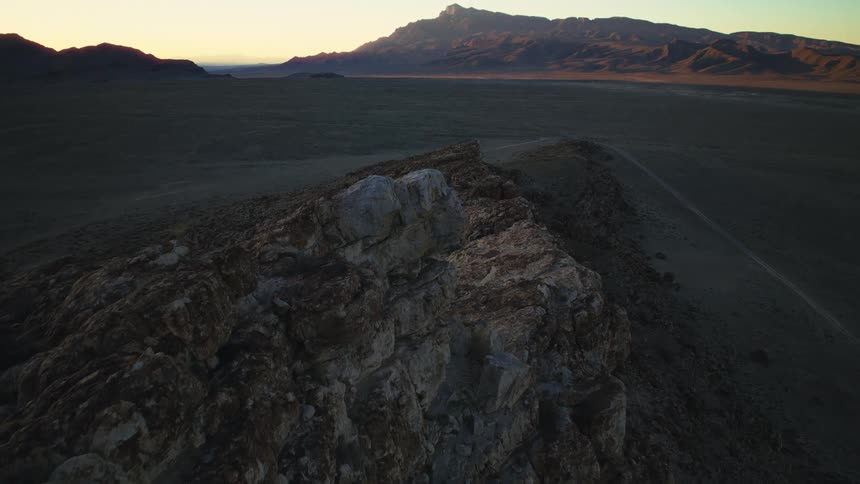 A slow push-in shot along a rugged, rocky ridge overlooking a vast desert landscape at sunrise