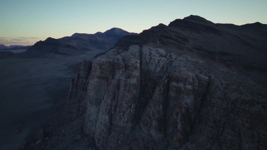 A slow aerial pan reveals a vast and rugged desert mountain range during the tranquil moments of dawn