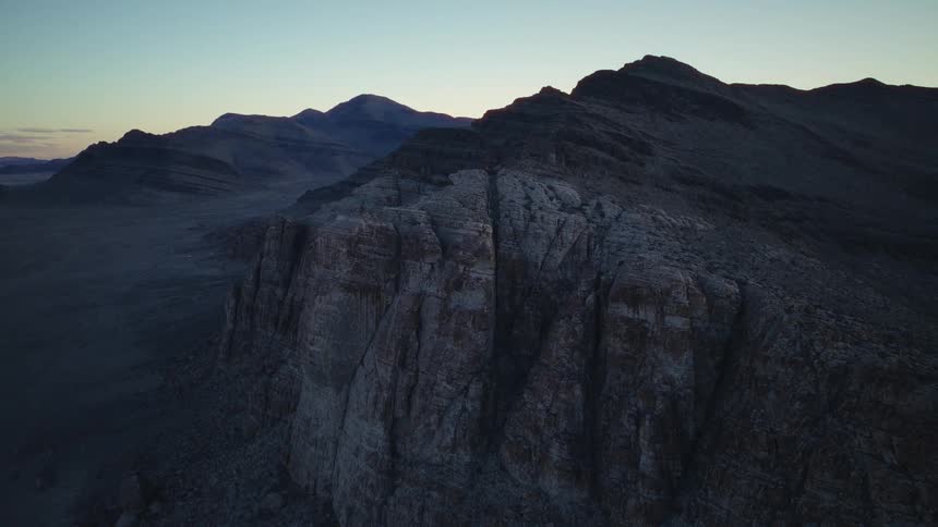 A slow aerial pan reveals a vast and rugged desert mountain range during the tranquil moments of dawn