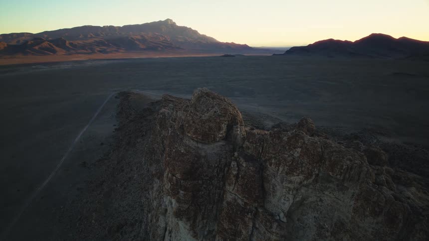 A slow aerial push-in shot over a rugged desert landscape with mountains in the distance at sunrise