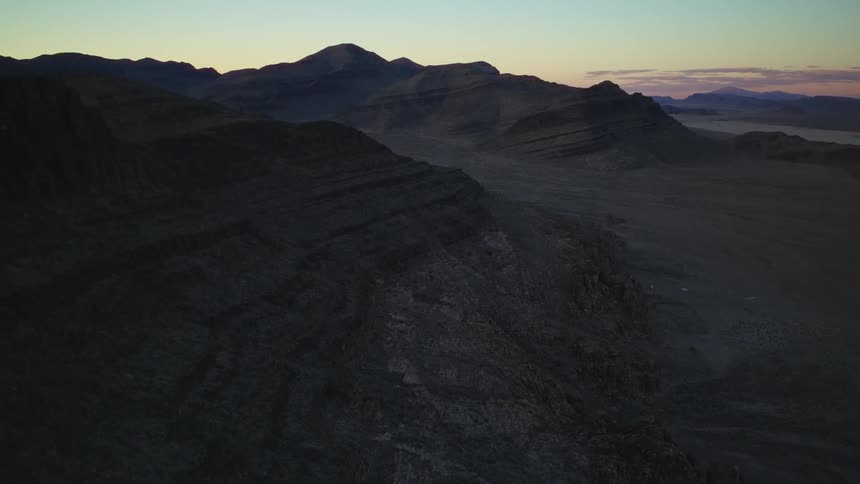 An atmospheric aerial view shows a vast and desolate mountain range in the deep shadows of twilight