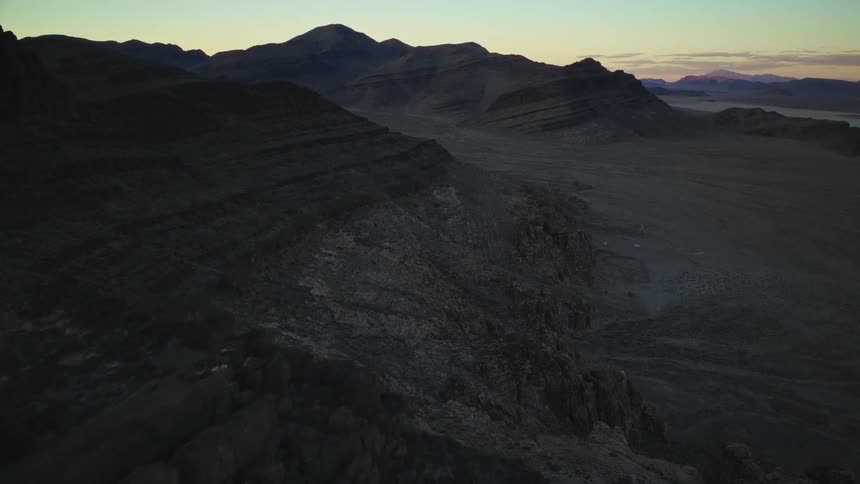 A beautiful time-lapse of the sun rising over a vast and rocky desert mountain range, casting long shadows across the valley