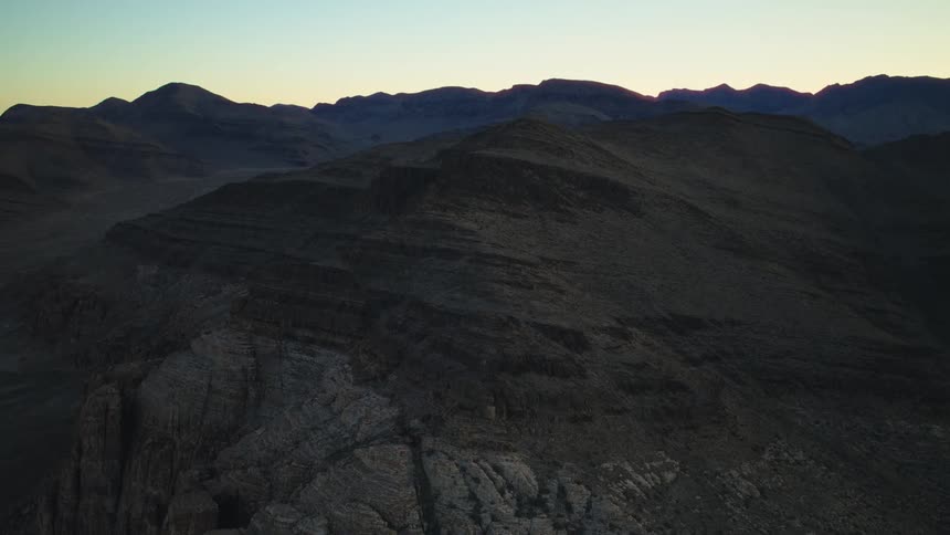 A serene aerial shot slowly pushes over a vast and rugged desert mountain range at twilight