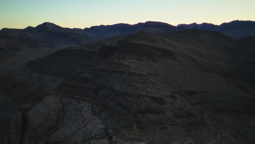 A serene aerial shot slowly pushes over a vast and rugged desert mountain range at twilight