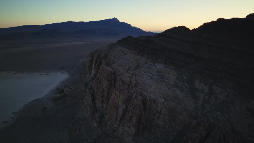Static aerial view of a rugged mountain ridge overlooking a vast desert plain at sunrise