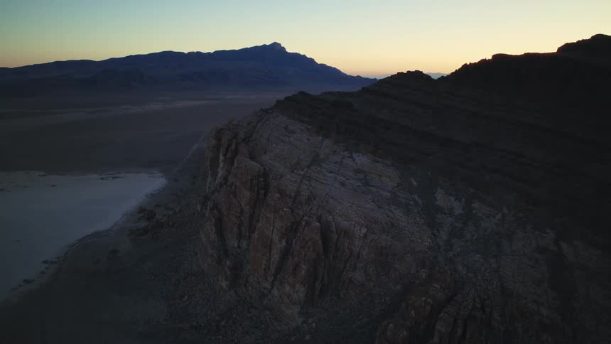Static aerial view of a rugged mountain ridge overlooking a vast desert plain at sunrise