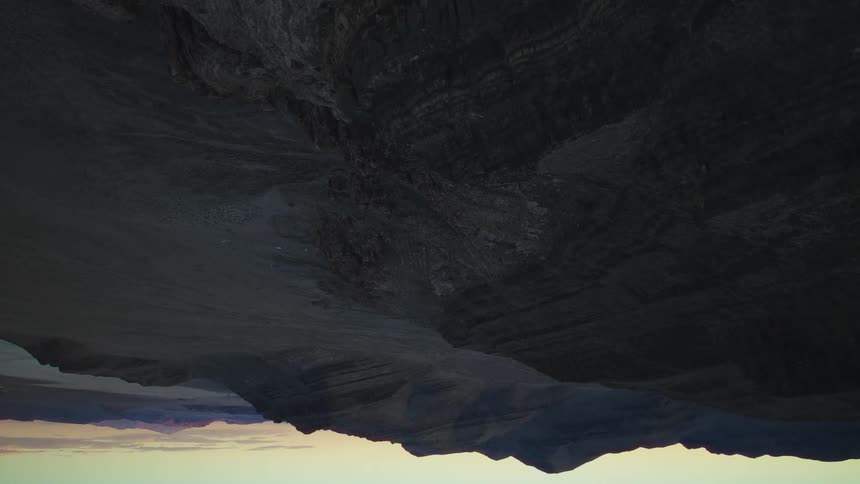 A surreal upside-down view of a barren mountain range silhouetted against a dusky sky