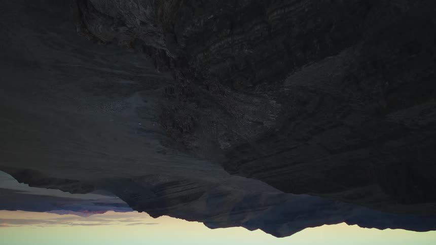 A surreal upside-down view of a barren mountain range silhouetted against a dusky sky