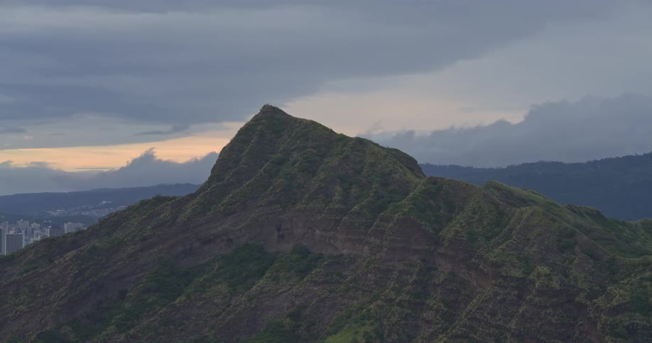 A slow zoom out from the peak of a lush green mountain ridge under a dramatic cloudy sky at dusk