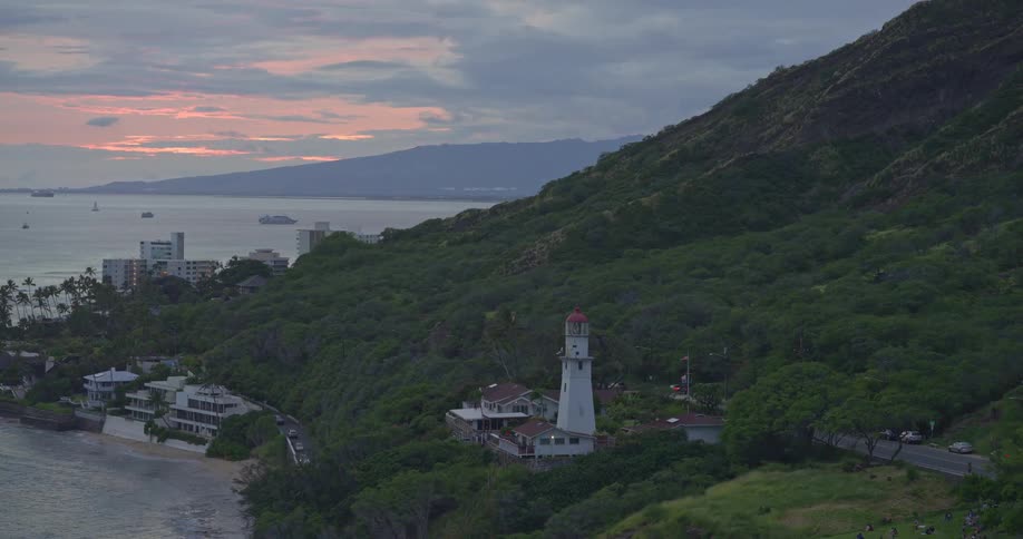 A serene aerial view of the Diamond Head Lighthouse on the coast of Oahu, Hawaii as its beacon shines at dusk
