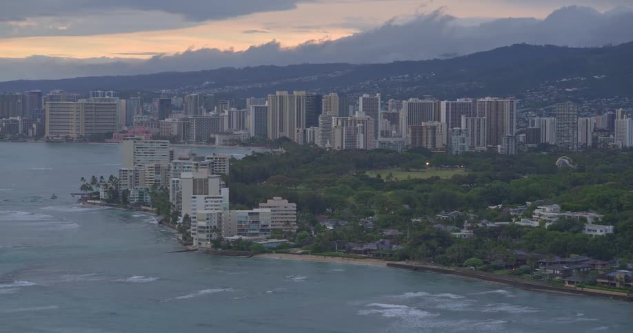 A panoramic aerial shot reveals the beautiful Waikiki coastline and Honolulu cityscape during a cloudy twilight