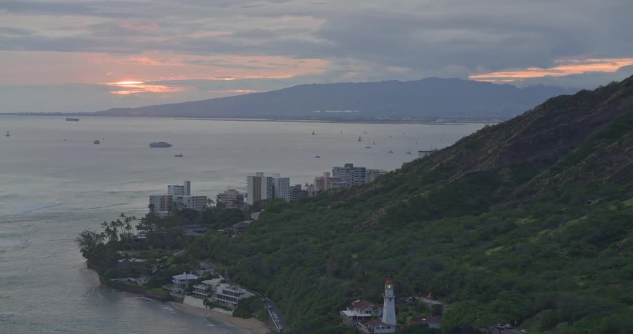 Aerial pullback reveals the Diamond Head Lighthouse along the Honolulu coastline at sunrise with boats on the water