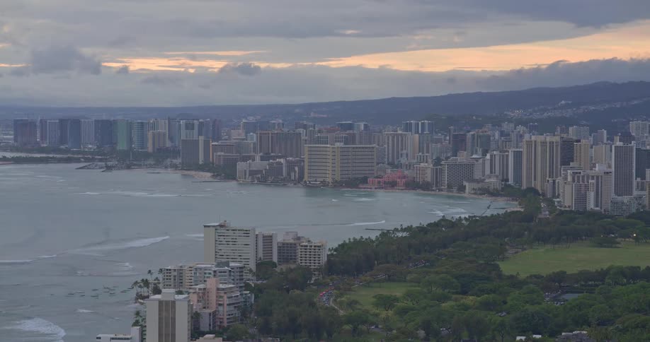 A scenic high-angle view of the Waikiki, Hawaii skyline and coastline at sunset under a cloudy sky